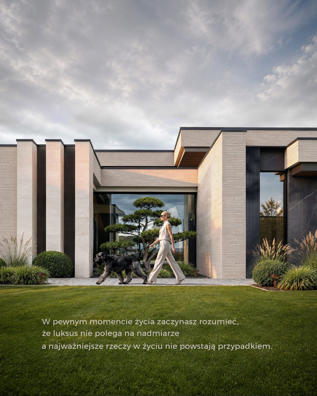Villa Horizon – kobieta z psem na ścieżce przed jasną elewacją z pionowymi podziałami, dużym przeszkleniem i formowanym drzewem.